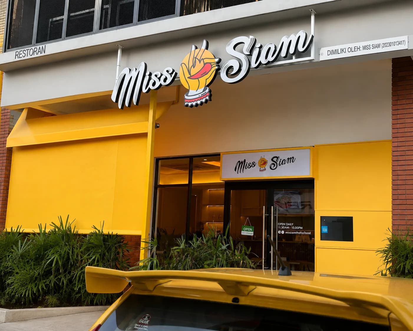 Shopfront of the Miss Siam Thai restaurant, with a bright yellow facade and illuminated script signage