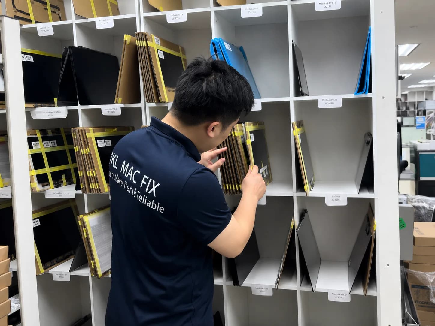 A YKL Mac Fix technician sorting MacBook parts in a labelled storage rack